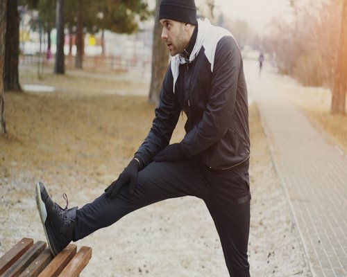 Man stretching his legs while sitting on a park bench during a lunch break